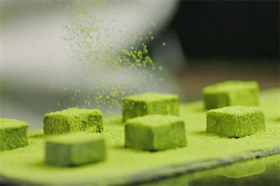 Matcha chocolate cubes being dusted with vivid green matcha powder for confectionery and CPG